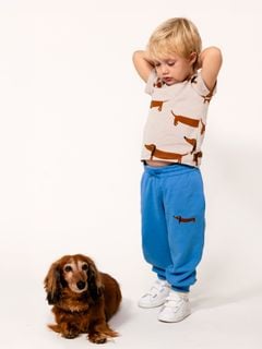 Front view of a child wearing blue sweatpants with a dog embroidery, standing next to a real dog.