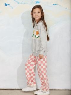 Pink and white chess check knitted trousers worn with a grey sweatshirt featuring a flower print panel.