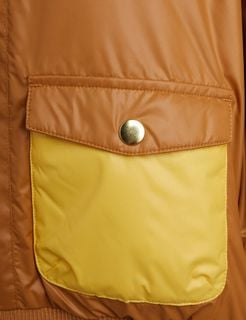 Close-up of a beige and yellow padded front pocket with a gold-tone snap button on a puffer jacket.