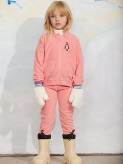 Pink zip-up jacket and trousers with penguin embroidery, worn with fluffy white mittens.