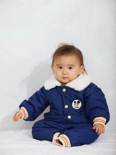 Blue quilted baby overall with a white faux-fur collar and Ritzratz patch, worn by a child.