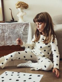 Child wearing an off-white long-sleeved top and matching trousers featuring a black dot print and a dog motif.