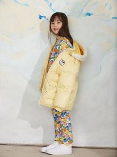 Yellow heavy puffer jacket with a Ritzratz patch and hood, worn over a floral outfit.