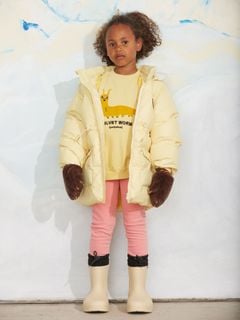 Yellow sweatshirt featuring a Velvet worm print, worn with a yellow puffer jacket and brown mittens.
