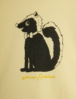 Close-up of a black and white skunk print wearing a bow tie on a yellow background with yellow Mini Rodini script.