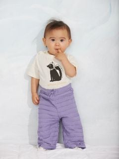 Off-white t-shirt featuring a Skunk print and shoulder snap buttons, worn with purple ruffled trousers.