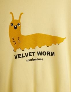 Close-up of a yellow sweatshirt featuring a smiling Velvet worm print and black text.