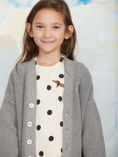 Grey melange knitted cardigan with button closure, worn over a dotted top.
