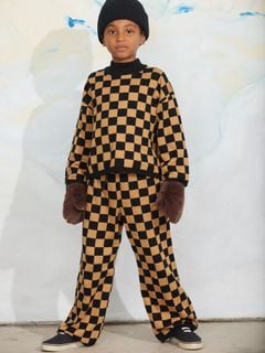 Brown and black Chess check knitted sweater with ribbed neck and cuffs, worn with matching trousers and furry mittens.