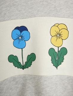 Close-up of a blue and a yellow Viola flower print on an off-white panel of a grey melange sweatshirt.