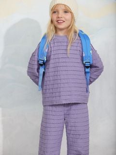 Purple textured frill trousers and matching top with scalloped edges, worn with a blue backpack.