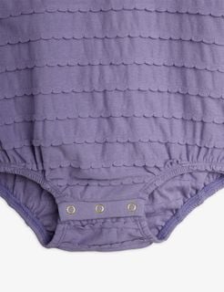 Close-up of a purple bodysuit featuring textured horizontal scalloped frills and snap buttons at the crotch.