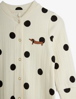 Close-up of an off-white ribbed jumpsuit with a black Dots print, snap-fastening buttons, and a brown dachshund dog patch.