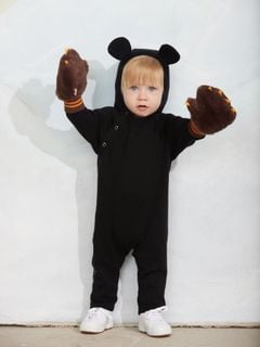 Black fine knit baby jumpsuit featuring a mouse-ear hood, snap buttons, and worn with brown fuzzy claw mittens.