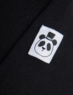 Close-up of a white brand label featuring a panda with a top hat on a black knit jumpsuit.