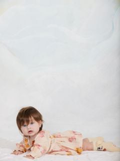 Kittens print bodysuit with a ruffled collar, worn by a baby lying on a light blue background.