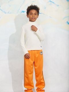 Orange Ritzratz patch trousers in recycled polyester with side piping, worn by a child with a cream turtleneck.