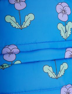 Close-up of blue padded fabric featuring a purple Violas print and quilted texture.