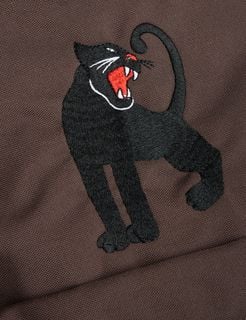Close-up of a detailed black panther embroidery with a red mouth on a brown fabric.