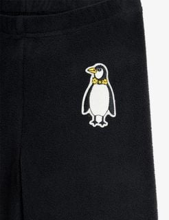 Close-up of a penguin patch with a yellow bow tie on black microfleece trousers.