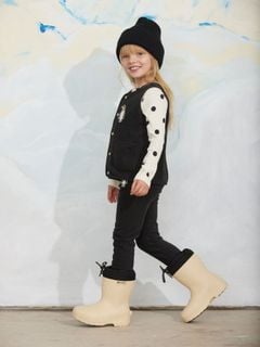 Black microfleece vest with penguin patch and front pockets, worn by a child walking in boots.