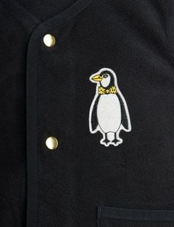 Close-up of a penguin patch and gold snap buttons on a black fleece vest.