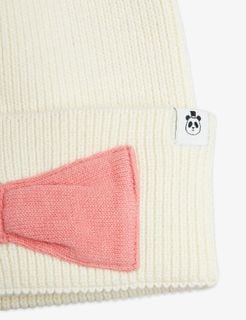 Close-up of an off-white ribbed beanie with a large pink bow and panda logo tag.