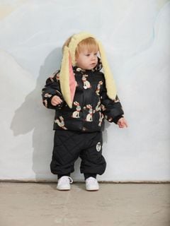 Black hooded puffer jacket with a rabbit print and fluffy bunny ear hood, worn by a child with quilted trousers.