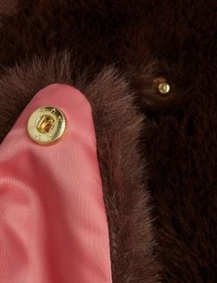 Brown faux fur jacket close-up showing a gold star-engraved snap button and coral lining.