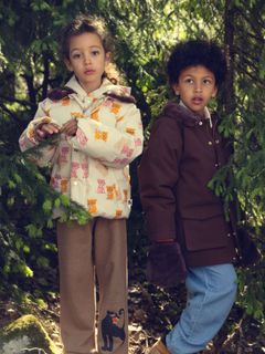 Brown padded parka with faux fur collar worn by a child standing outdoors among trees.