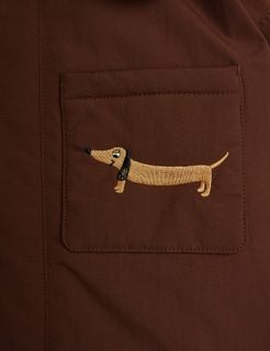 Close-up of a brown parka pocket with a detailed beige and black dachshund embroidery.
