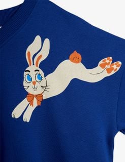 Rabbits print of a leaping white rabbit with an orange bow on a blue sweatshirt.