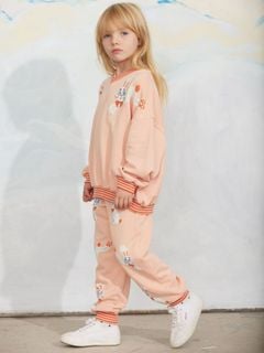 Pink sweatshirt and matching trousers with a Rabbits print and striped ribbed trims, worn by a child.