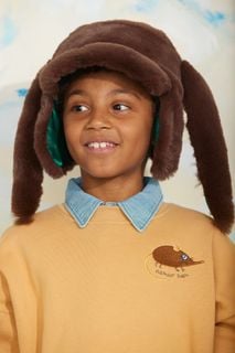 Child wearing a beige sweatshirt with an embroidered elephant shrew and a brown fluffy aviator hat.