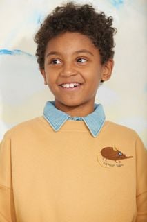 Close-up of a child wearing a beige sweatshirt with an embroidered Elephant shrew and a light blue collar.