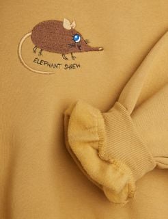 Beige sweatshirt close-up with a ribbed cuff and brown Elephant Shrew embroidery.