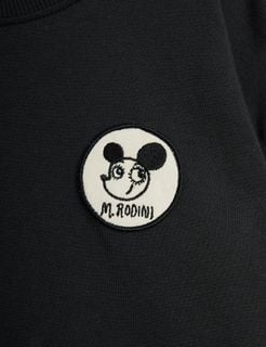 Circular white patch featuring a Ritzratz motif and black text on a black long-sleeved top.