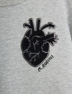 Close-up of a black anatomical heart application and M. Rodini embroidery on grey melange fabric.