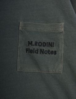 Close-up of a grey chest pocket featuring dark M.RODINI Field Notes embroidery.