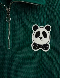 Close-up of green chunky knit sweater featuring a silver half-zip and a Panda patch.