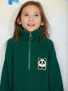 Close-up of a green chunky knit half-zip sweater with a panda patch on the chest, worn by a child.