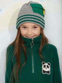 Green chunky-knitted half-zip sweater with panda patch and high collar, worn by a child wearing a striped hat.