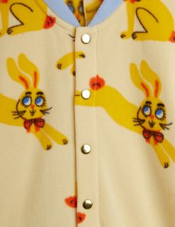 Yellow fleece bodysuit close-up featuring a Rabbits print and gold-toned snap button closure.