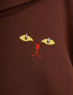 Yellow cat eyes and an orange nose and mouth print on a brown hoodie.