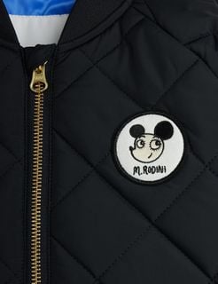 Close-up of a black quilted puffer jacket featuring a round Ritzratz character patch and gold zipper.