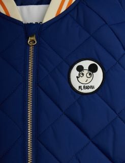 Close-up of a blue quilted puffer jacket featuring a round Ritzratz patch and a golden metal zipper.