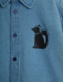 Close-up of a blue denim shirt featuring a black skunk motif wearing a bowtie and button closure.