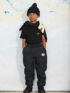 Black short-sleeved t-shirt with a chest pocket and elephant shrew embroidery, worn by a child with quilted trousers.