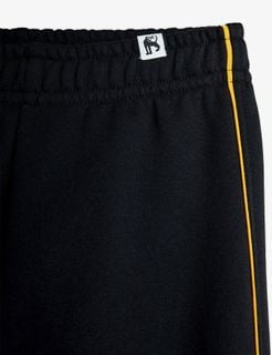 Close-up front view of black sweatpants featuring yellow piping and an elastic waistband.