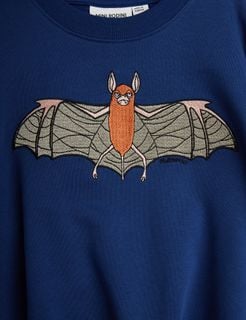 Close-up of a blue sweatshirt featuring an embroidered orange bat with spread wings.